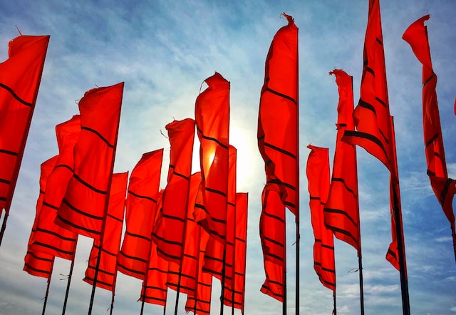 Several red flags flying against a blue sky.