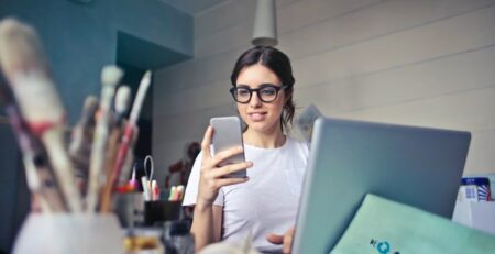 A social media manager works on both her phone and her laptop. 