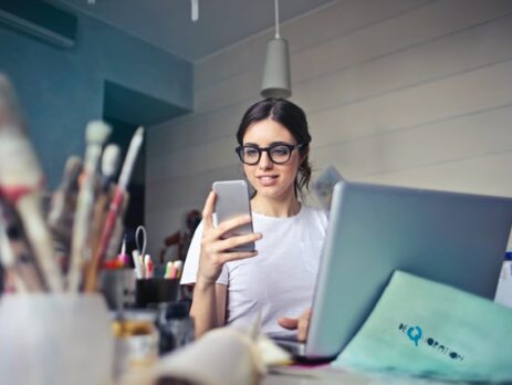 A social media manager works on both her phone and her laptop. 