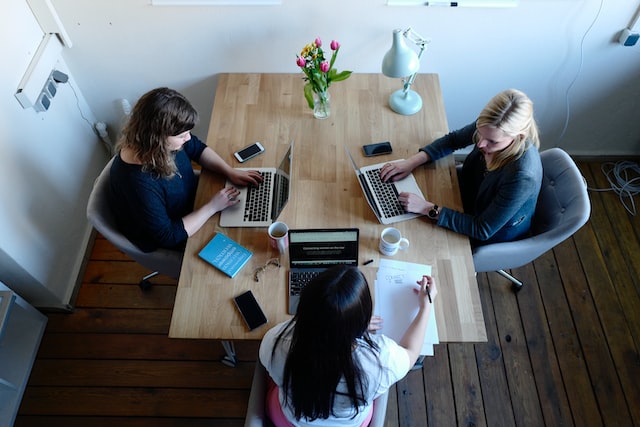 A team of three women work on computers around a table. 