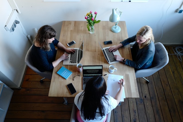 A team of three women work on computers around a table.
