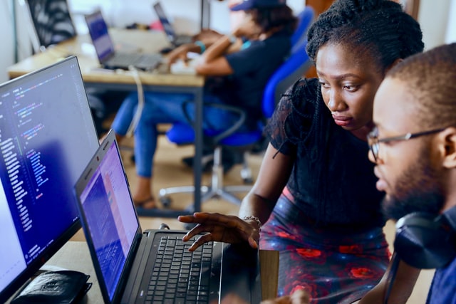 A woman shows a man how to code something on a laptop computer. 