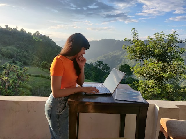 A dark-haired woman works at a standing desk in nature. 