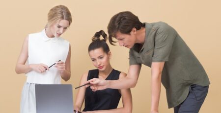 Three people discuss working together on a laptop computer. 