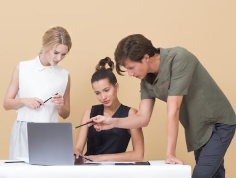 Three people discuss working together on a laptop computer. 