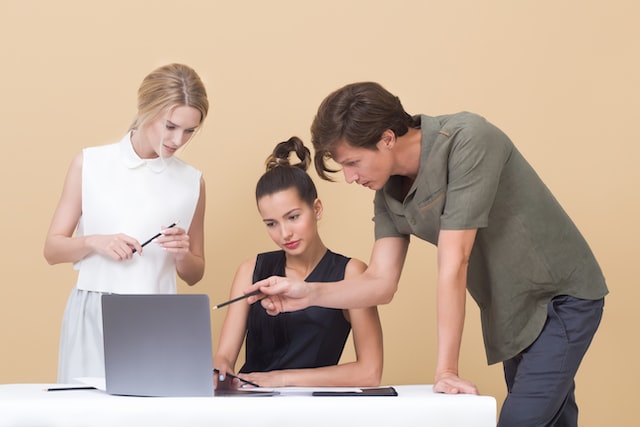 Three people discuss working together on a laptop computer. 