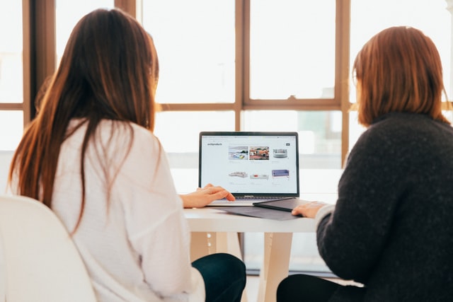 Two women work on software on a computer.