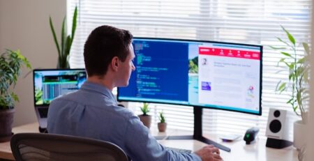 A man works on software on a dual-screen computer. 