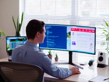 A man works on software on a dual-screen computer. 