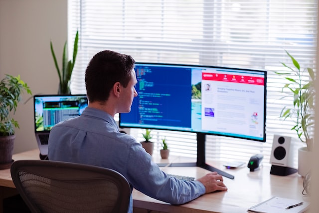 A man works on software on a dual-screen computer. 