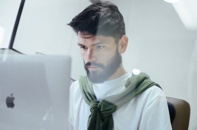 A dark haired man works on a laptop.