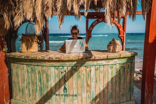 A dark haired woman works from her laptop in a tropical location.