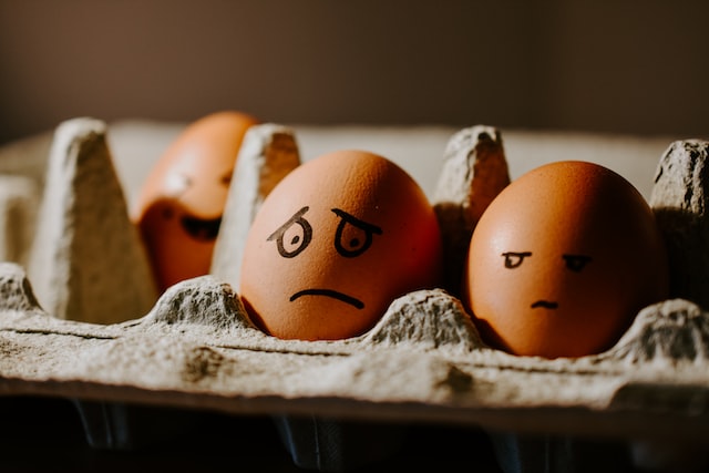Two eggs are in a carton and have sad faces on them. 