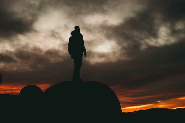 A man stands on a rock and looks out over the landscape in fading light. 