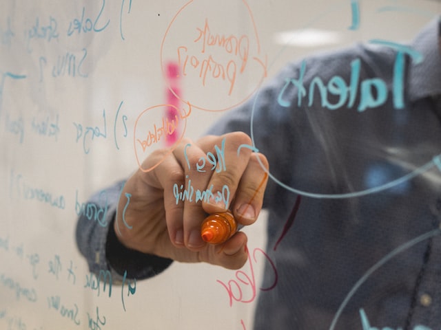 A hand writes on a glass board with a colored marker.