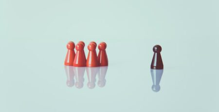 A group of red pawns is across from a brown pawn on a white backdrop.