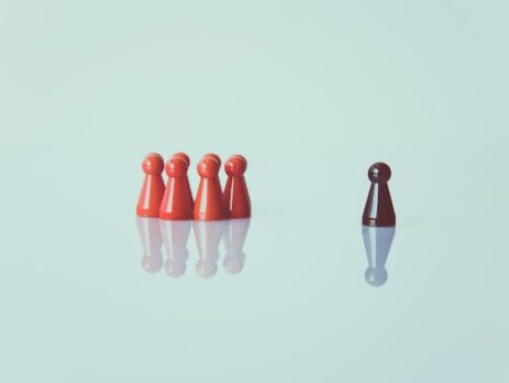 A group of red pawns is across from a brown pawn on a white backdrop.