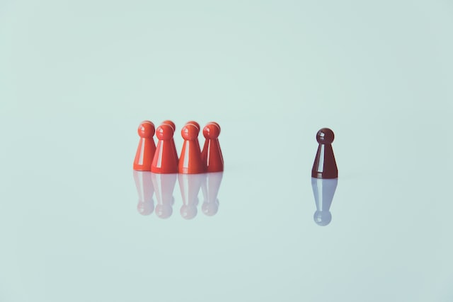 A group of red pawns is across from a brown pawn on a white backdrop.