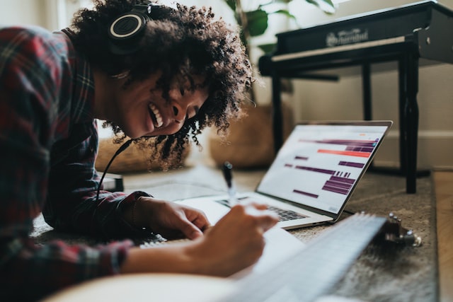 A black woman works on a laptop on the floor.