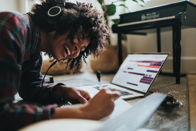 A black woman works on a laptop on the floor. 