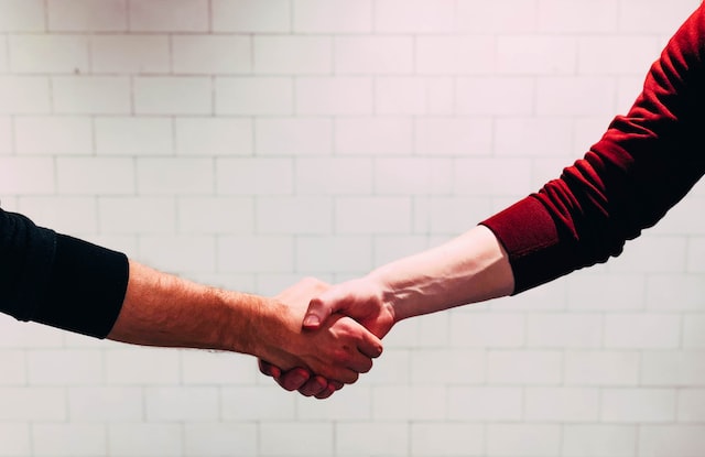 Two people shake hands against a white background.