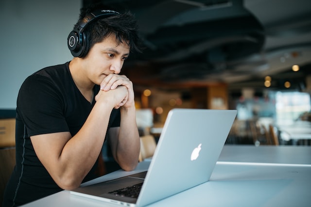 A man wears headphones and looks at a laptop screen. 