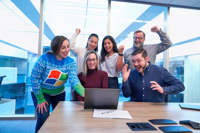 A group of people look at a laptop computer and cheer in the workplace. 