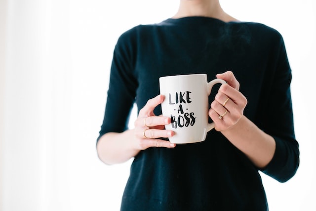 A woman holds a coffee mug that says like a boss. 
