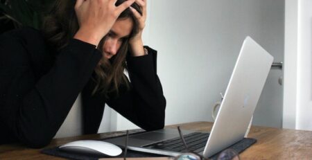 A woman is in front of her laptop with her head in her hands. 