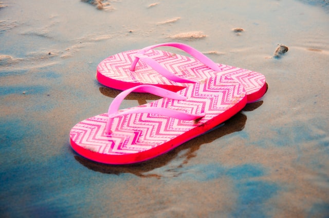 Pink flip-flops sit on the beach. 