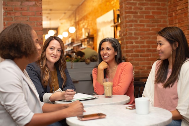 A group of women sit around a table and talk.