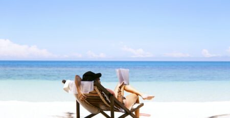 A woman sitting on a beach chair on the beach reads a book. 