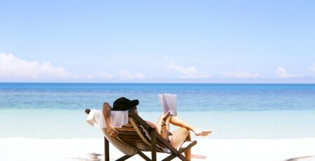 A woman sitting on a beach chair on the beach reads a book. 