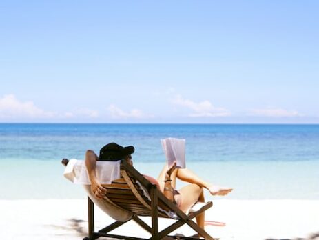 A woman sitting on a beach chair on the beach reads a book. 