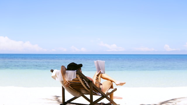 A woman sitting on a beach chair on the beach reads a book. 