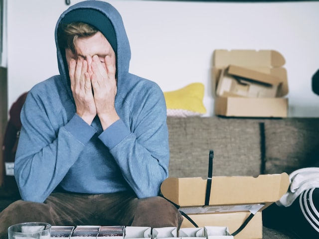 A man in a hoodie covers his face with his hands.