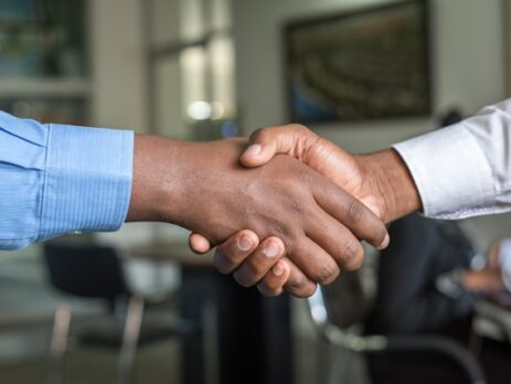 Two men shake hands in front of a blurred background.