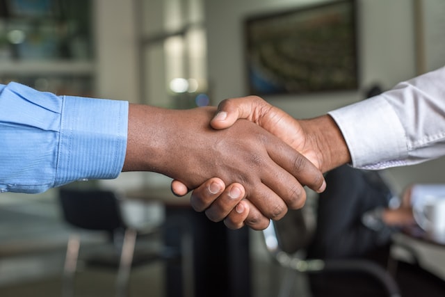 Two men shake hands in front of a blurred background. 