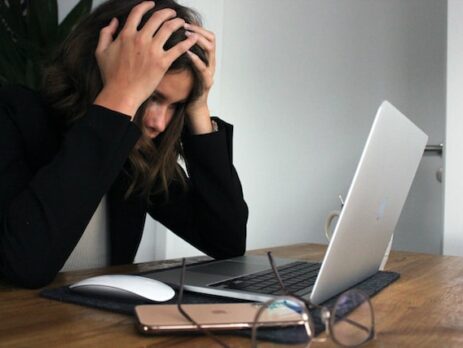 A woman is in front of her laptop with her head in her hands.