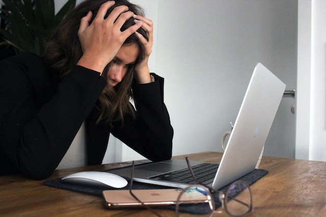 A woman is in front of her laptop with her head in her hands.