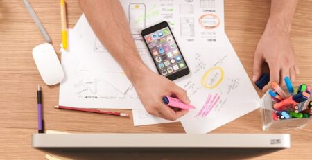 A desk with papers, a phone, and an individual highlighting items. 