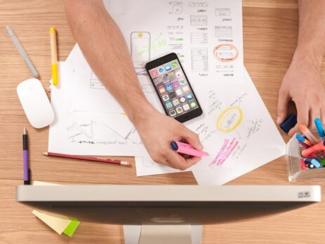 A desk with papers, a phone, and an individual highlighting items. 