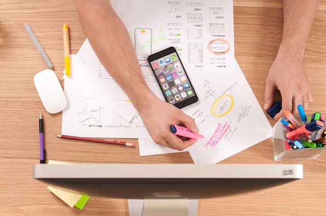 A desk with papers, a phone, and an individual highlighting items. 