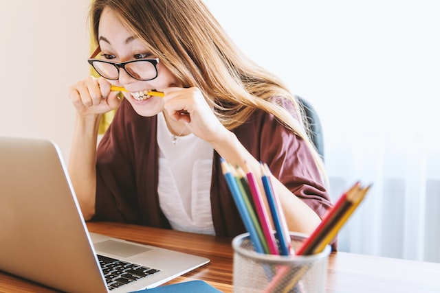 A woman bites her pencil as she looks at her computer. 