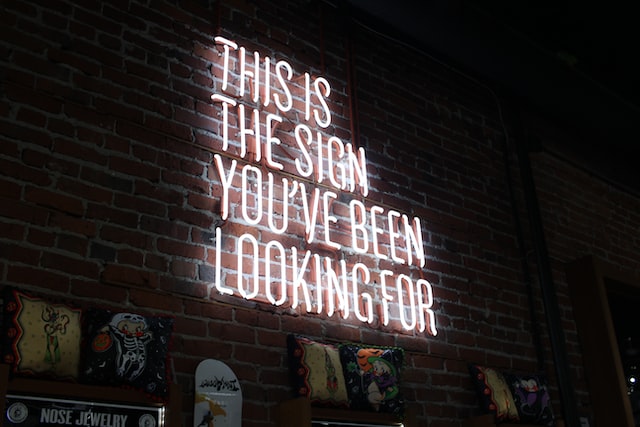 A white sign with the words “this is the sign you have been looking for” is illuminated against a brick background