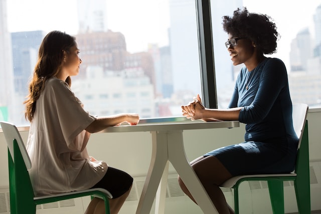 One woman interviews another while sitting at a table