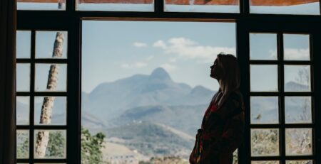 A woman looks out a window into nature as she considers a decision. 