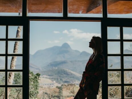 A woman looks out a window into nature as she considers a decision. 