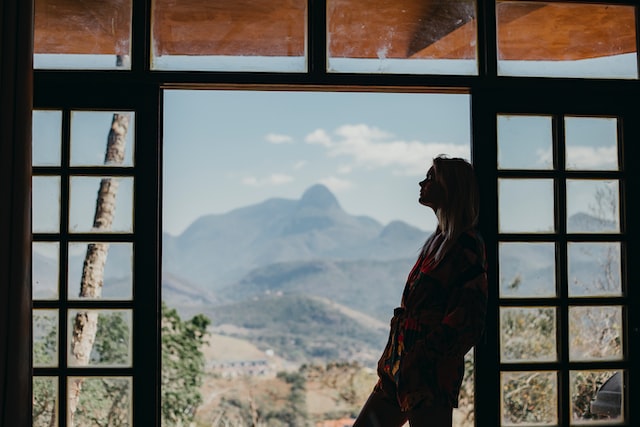 A woman looks out a window into nature as she considers a decision. 