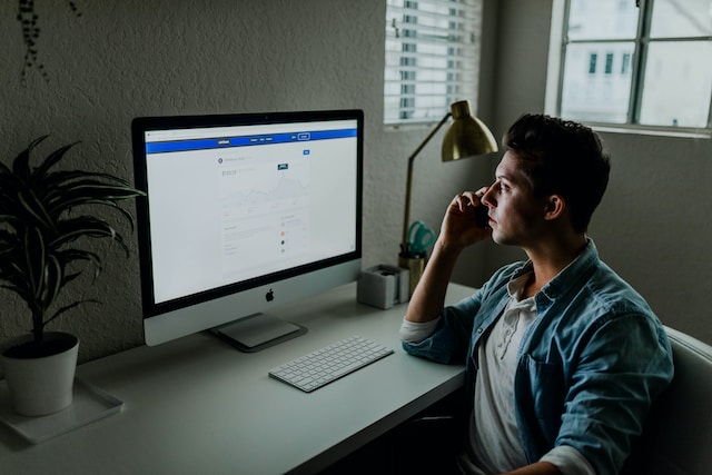 A man works on a large computer with Facebook on the screen.